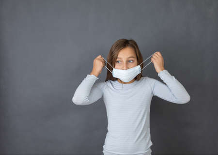 Portrait of a young girl puttin on medical mask on grey background.の写真素材