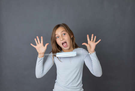 Portrait of young teen girl giving up with medical mask on her hands on grey background.の写真素材