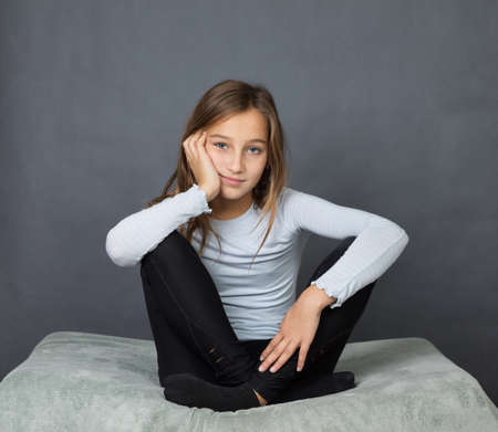 Portrait of a young girl sitting on pillow with hand on her face on grey background with space for textの写真素材