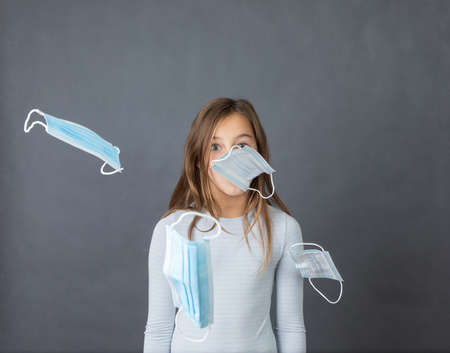 Portrait of a young scared girl with flying medical masks all over her face on grey background.の写真素材