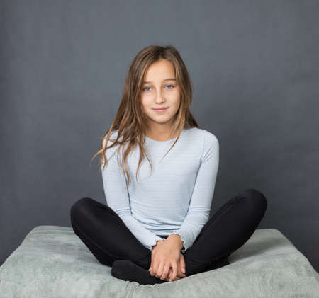 Portrait of a young girl sitting on pillow on grey background with space for textの写真素材