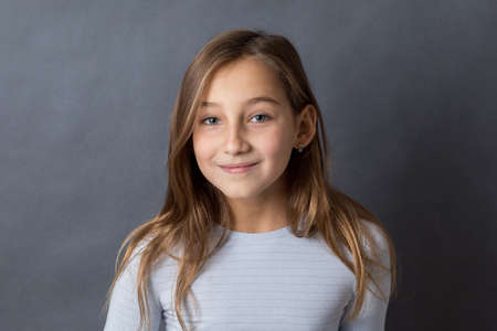 Portrait of a young happy slightly smiling girl on grey background with space for textの写真素材