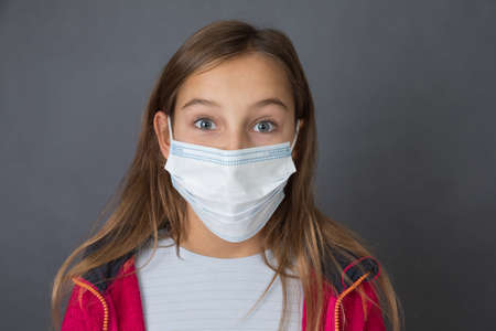 Portrait of a young girl in red sweater in medical mask on grey background.の写真素材
