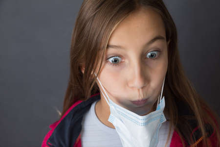 Closeup portrait of a young girl with read sweater in a medical mask on grey background.の写真素材