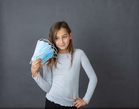 Portrait of a young happy girl playing with medical mask on grey background.の写真素材