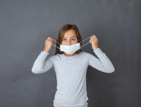 Portrait of a young girl putting on medical mask on grey background.の写真素材