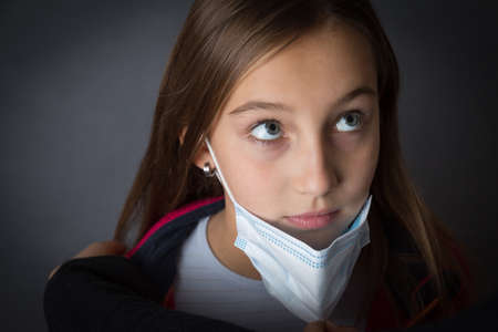Closeup portrait of a young girl with read sweater in a medical mask on grey background.の写真素材