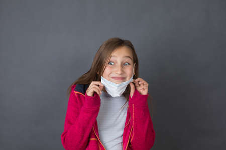 Portrait of a young girl in red sweater playing with medical mask on grey background.の写真素材