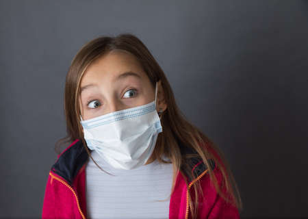 Portrait of a young girl with read sweater in a medical mask on grey background.の写真素材