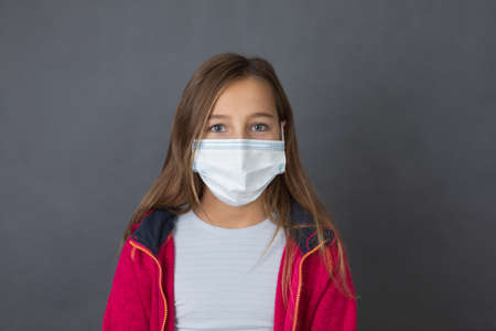 Portrait of a young girl with read sweater in a medical mask lookig in to camera on grey background.の写真素材