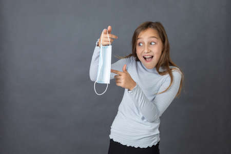 Portrait of a young scared girl playing with medical mask on grey background.の写真素材