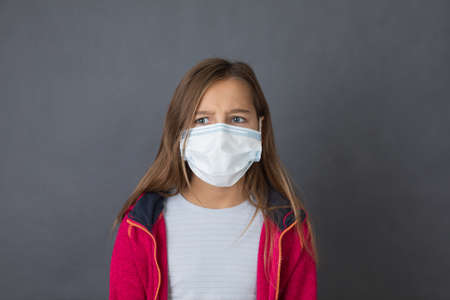 Portrait of a young girl in red sweater in medical mask on grey background.の写真素材