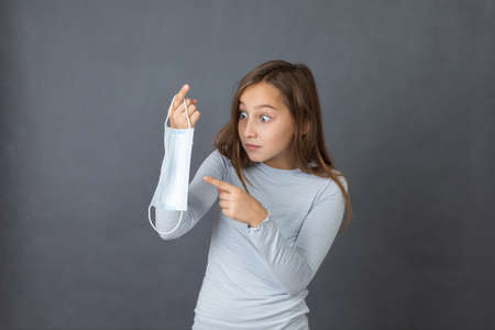 Portrait of a young angry girl playing with medical mask on grey background.の写真素材