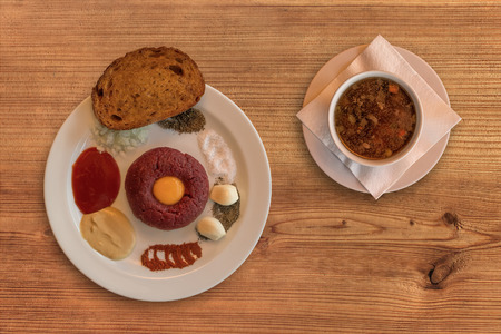 Flat lay of raw beef . Tasty Steak tartare. Classic steak tartare on rustic wooden table with a beef broth. Ingredients: Raw beef meat, salt, pepper, onion, caraway, mustard, tomato pyre, egg, garlic, toast or fried bread.の写真素材
