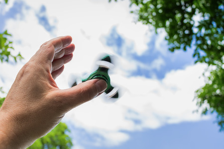 Male hand with rotating fidget spinner against skyの写真素材