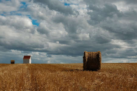 Wheat field in summer. After the harvest. With bales of straw in front of a dramatic sky and a small chapel.の写真素材