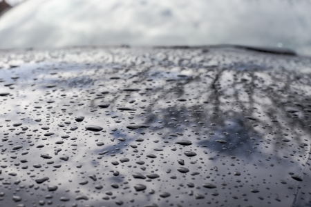 water drops on a black car hood with reflection on itの写真素材