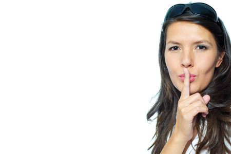 Woman making a shushing gesture raising her finger to her lips as she requests silence or asks the viewer to share her secret, head and shoulders portrait with copyspace alongsideの写真素材