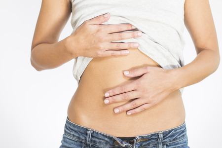 Woman with her monthly menstrual pains clutching her stomach with her hands as she becomes stressed by the ongoing cramps, torso view of her hands and tummy isolated on whiteの写真素材