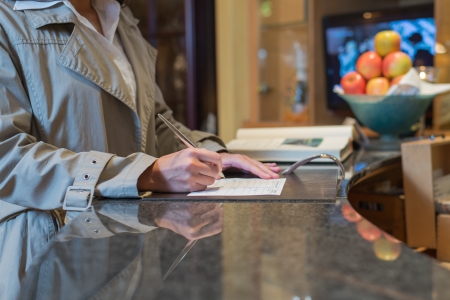 female hotel guest filling in registration form upon checking in, service and tourism conceptの写真素材
