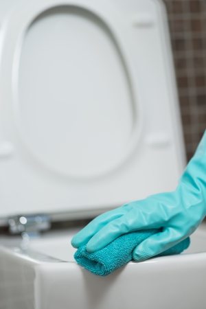 Hand of a person cleaning the toilet seat in rubber gloves with a sponge disinfecting the underside for germs and bacteria while performing household choresの写真素材