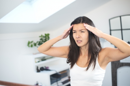 Attractive young woman with a migraine headache standing holding her fingers to her temples with her eyes half closed in painの写真素材