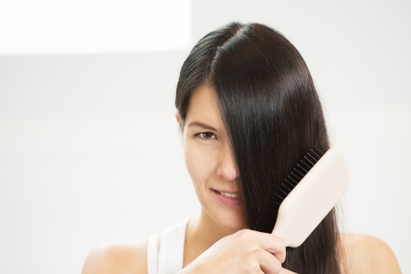 Attractive woman brushing her hair with one eye concealed by her long brunette locks looking at the camera with a sensual seductive lookの写真素材