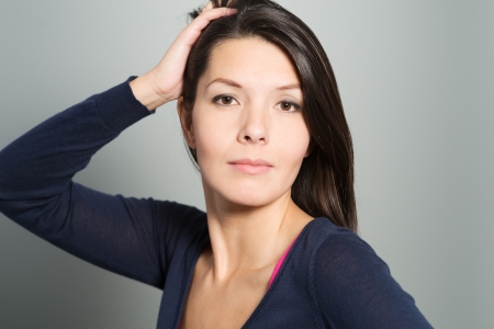 Thoughtful attractive woman with a serene face and enigmatic smile standing with her hand to her chin looking pensively at the cameraの写真素材