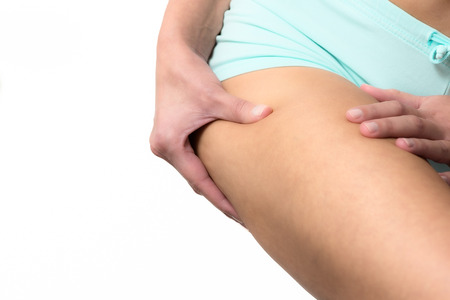 Slender young woman checking for excess weight on her thighs pinching the muscle between her hands,...