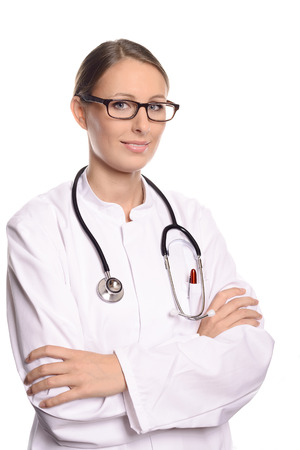 Smiling confident female doctor or nurse wearing glasses standing with folded arms in a white lab coat with a stethoscope around her neck isolated on whiteの写真素材