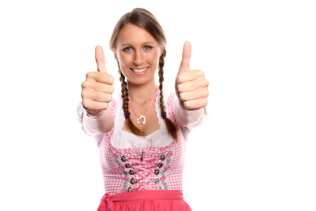 Happy young woman in a pinkish dirndl giving a thumbs up, symbol for success and happiness, Oktoberfest concept isolated on whiteの写真素材