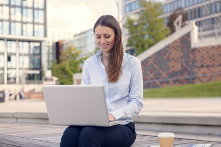 Attractive young woman wearing formal clothes while working outdoor on a laptop, with a wireless connection to the internet, in a nice day of summerの写真素材