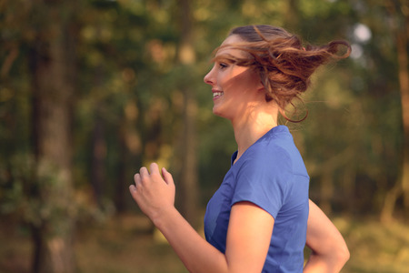 Close up side view of a happy smiling young woman jogging in the countryside as she gets her daily exercise in a health and fitness conceptの写真素材