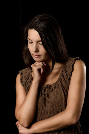 Melancholy depressed young woman with a serious expression and downcast eyes standing thinking in a deep contemplation with her hand to her chinの写真素材