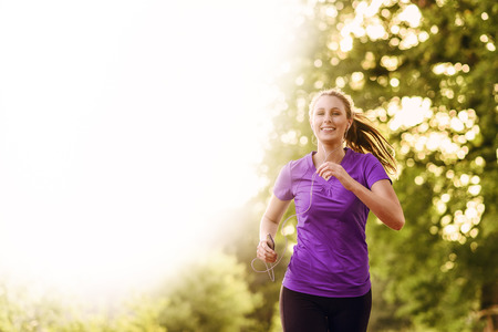 Woman listening to music on her earplugs and MP3 player while jogging along a country road in a healthy lifestyle, exercise and fitness conceptの写真素材