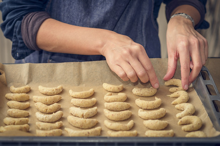 Cook preparing traditional crescent biscuits for Christmas and the festive season arranging the dough ready for cooking on a large oven or baking tray , close up of the handsの写真素材