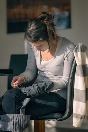 Young housewife or mother stitching darning a pair of jeans trousersの写真素材