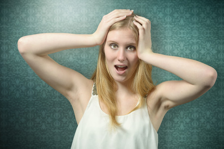 Close up Shocked Woman with Blond Hair Holding her Head While Looking at Camera, on green background