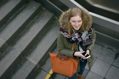 Aerial Shot of a Stylish Young Woman in Winter Fashion with Mobile Phone and Leather Bag, Pause for a Moment at the Stairs While Looking at the Camera.の写真素材