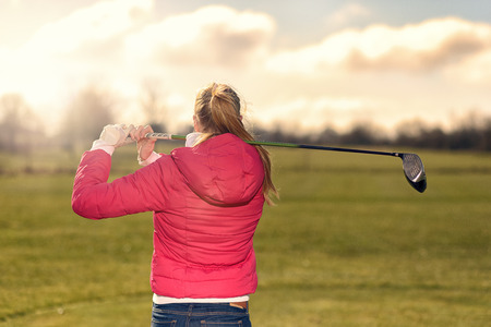 Female golfer watching her drive from the tee  after making a stroke staring down the fairway with her driver club resting on her shoulder, view from behindの写真素材