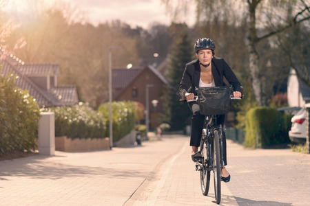Young businesswoman riding to work on a bicycle along a residential street in her stylish slack suit and safety helmet in an eco-friendly mode of transportの写真素材