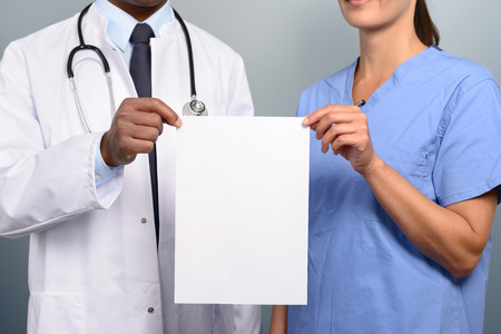 Close up torso view of a doctor and nurse holding up a blank white sign with copyspace for your medical alert, announcement or promotion in a healthcare conceptの写真素材