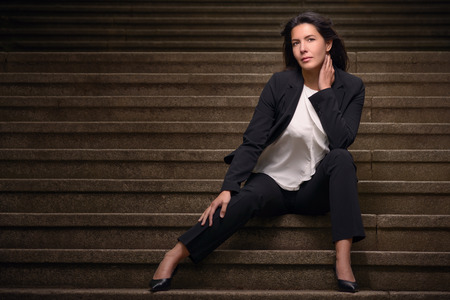 Attractive brunette woman in a slack suit sitting on urban stairs looking at camera in a sensual way, with copy spaceの写真素材