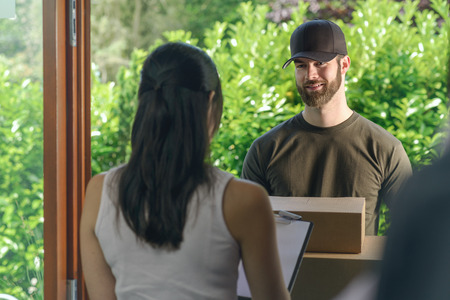Woman accepting a delivery of two cardboard boxes with an order or gift signing the clipboard for the friendly smiling deliveryman on the doorstepの写真素材