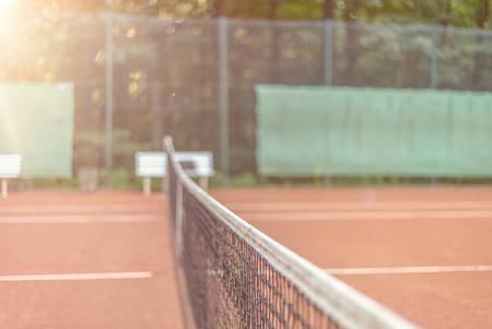 View across the length of the net on an all-weather tennis court towards side fencing with adverts, court is empty conceptual of sport, championships and tournamentsの写真素材