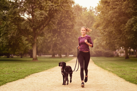 Full length Shot of a Healthy Young Woman Jogging in the Park with her Black Pet Dogの写真素材