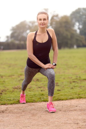Athletic young woman in sportswear doing stretching exercises outdoors on a track to warm up her muscles before doing a training workout, health and fitness conceptの写真素材