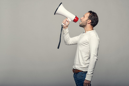Man speaking over a megaphone as he makes a public address, participates in a protest or organises a rally or promotion, over grey with copy space to the sideの写真素材