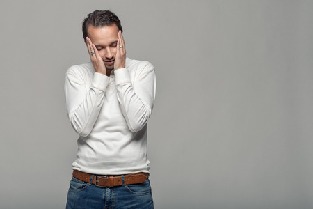 Half Body Shot of a Thoughtful Young Man Touching his Face with Eyes Closed Against Gray Background...