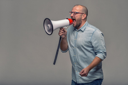 Man speaking over a megaphone as he makes a public address, participates in a protest or organises a rally or promotion, over grey with copy space to the sideの写真素材